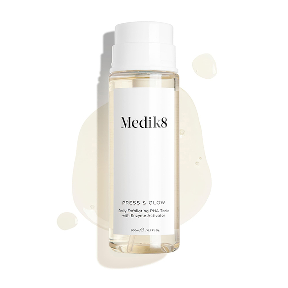 Medik8 Press & Glow tonic bottle stands against a clean white background with translucent liquid droplets and a puddle, highlighting its watery texture. Text identifies the product as a 200mL "Daily Exfoliating PHA Tonic with Enzyme Activator."-35