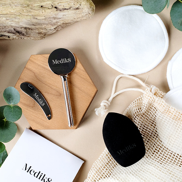 Une composition à plat d’accessoires éco Medik8 sur un fond beige, comprenant un presse-tube en métal, une spatule en métal, des cotons en bambou réutilisables, un sac en filet et une éponge de maquillage noire.-hover-45