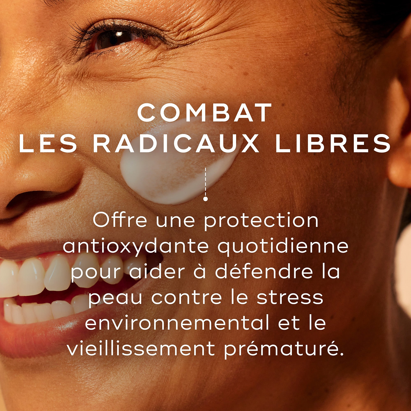 Gros plan sur le visage souriant d'un mannequin avec une trace de crème blanche appliquée sur sa joue. Le texte Combat les radicaux libres explique qu'il offre une protection antioxydante quotidienne pour aider à défendre la peau contre le stress environnemental et le vieillissement prématuré.