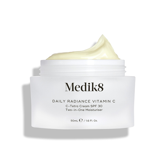 Een open glazen pot Medik8 Daily Radiance Vitamin C wordt getoond met een royale toef lichtgele crème bovenop. De tekst identificeert het product als een 50 ml C-Tetra Cream SPF 30, een twee-in-één moisturizer.-22