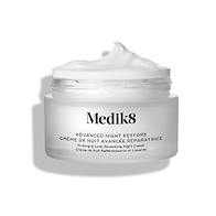 Słoiczek z kremem Medik8 Advanced Night Restore przedstawiony w pozycji otwartej, z obfitą porcją białego kremu uformowaną w kopczyk na wierzchu, na tle czystej bieli, co podkreśla jego gładką, regenerującą konsystencję. Na słoiczku widnieje czarny napis: „Rejuvenating Multi-Ceramide Night Cream”.