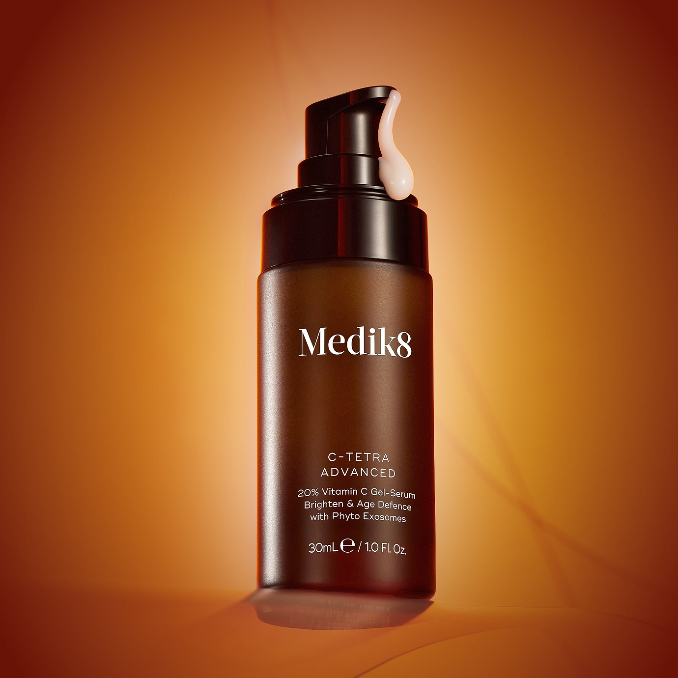 A bottle of Medik8 C-Tetra Advanced serum with a pump, set against a warm orange background. A drop of milky serum hangs from the nozzle. Text highlights 