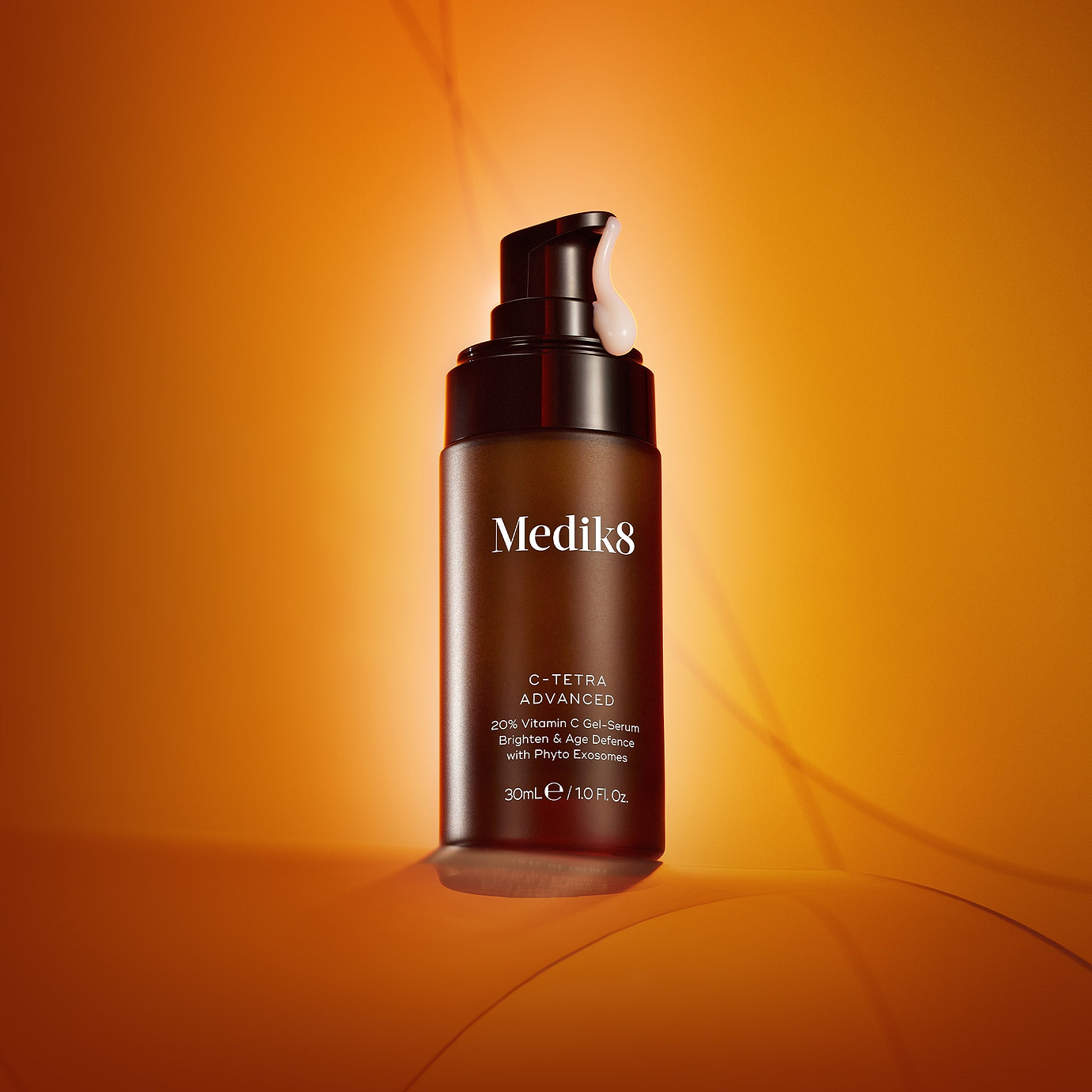 A product photo of the Medik8 C-Tetra Advanced serum. The brown bottle is spotlit against a vibrant, glowing orange background. The label reads: 