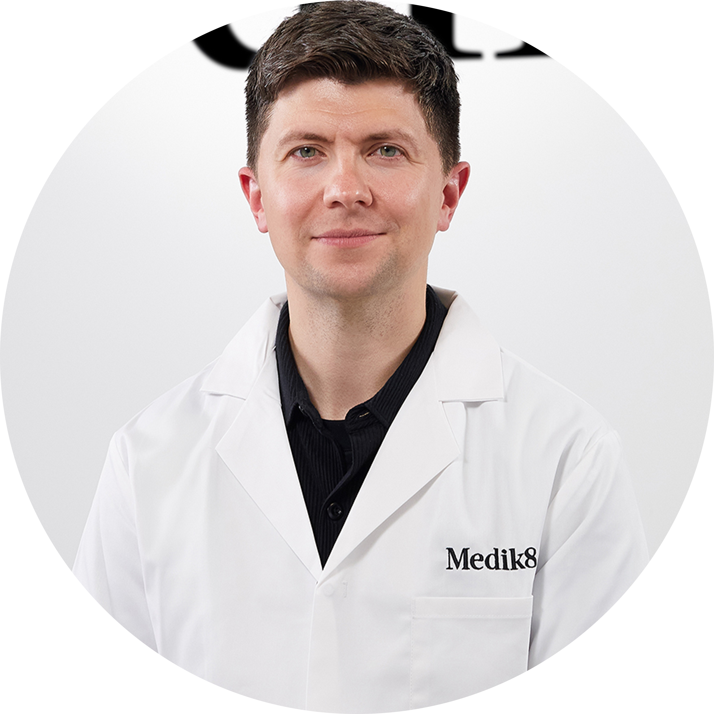 A circular headshot of a smiling man wearing a white Medik8 branded lab coat over a black shirt, set against a clean white background.