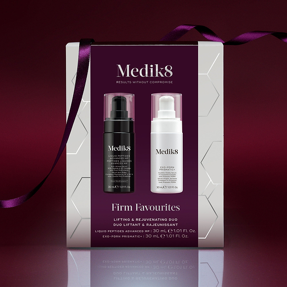 A Medik8 "Firm Favourites" gift box wrapped with a purple ribbon, set against a deep burgundy background with a reflective surface. The white box features a burgundy center panel displaying a Liquid Peptides Advanced MP black pump bottle and an Exo-PDRN Prismatic+ white pump bottle inside.-1
