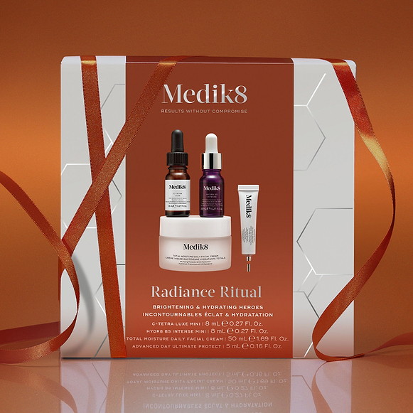 A Medik8 "Radiance Ritual" gift box wrapped with an orange ribbon against a burnt orange background. The white box features a burnt orange centre panel displaying a printed C-Tetra Luxe mini serum bottle, Hydr8 B5 Intense mini serum bottle, Total Moisture Daily Facial Cream jar, and Advanced Day Ultimate Protect deluxe sample tube. Text highlights "Brightening & Hydrating Heroes."-2