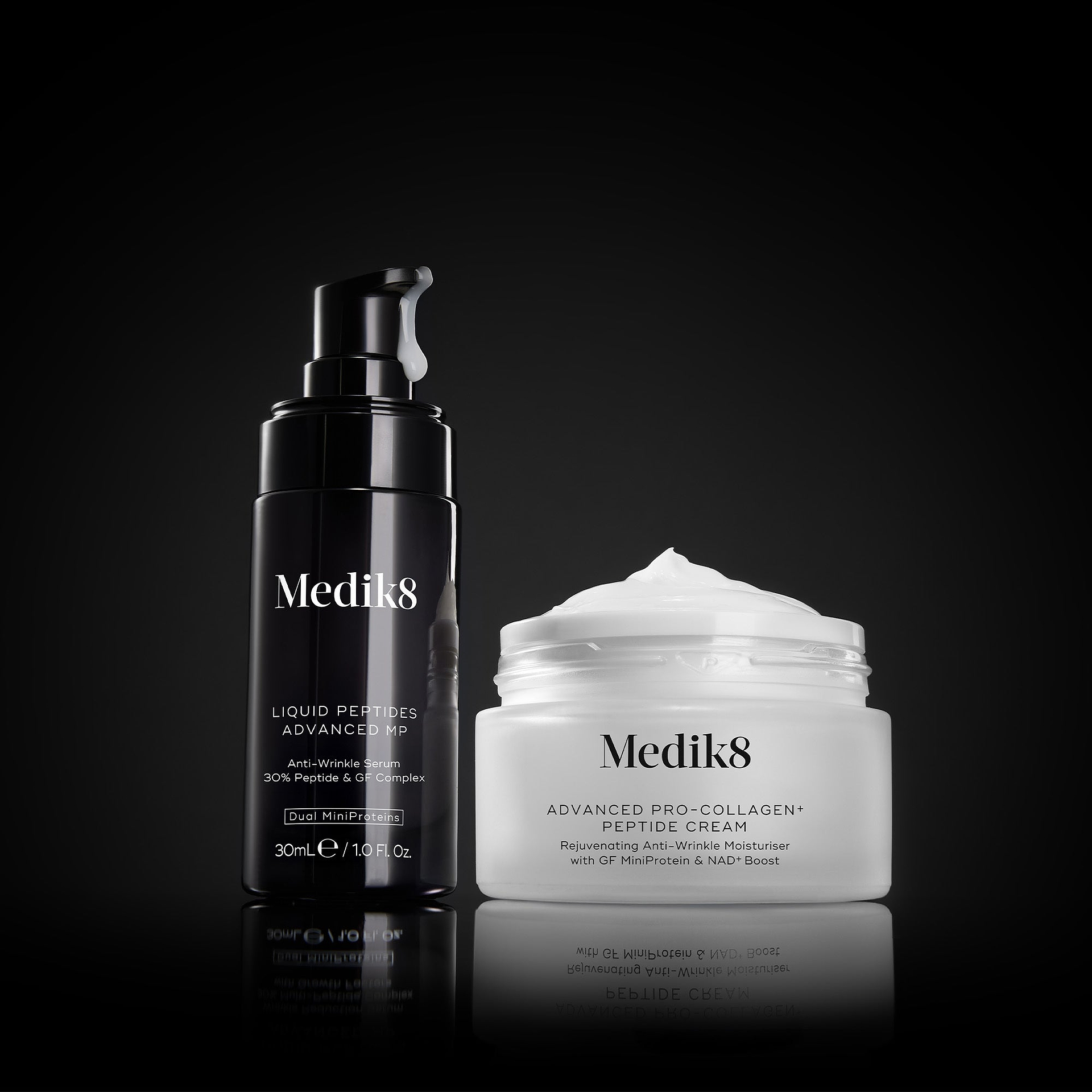 A black Medik8 Liquid Peptides Advanced MP pump bottle with a falling drop of serum alongside an open white Advanced Pro-Collagen+ Peptide Cream jar displaying its texture. They rest on a reflective black surface against a dark background. Text highlights the serum