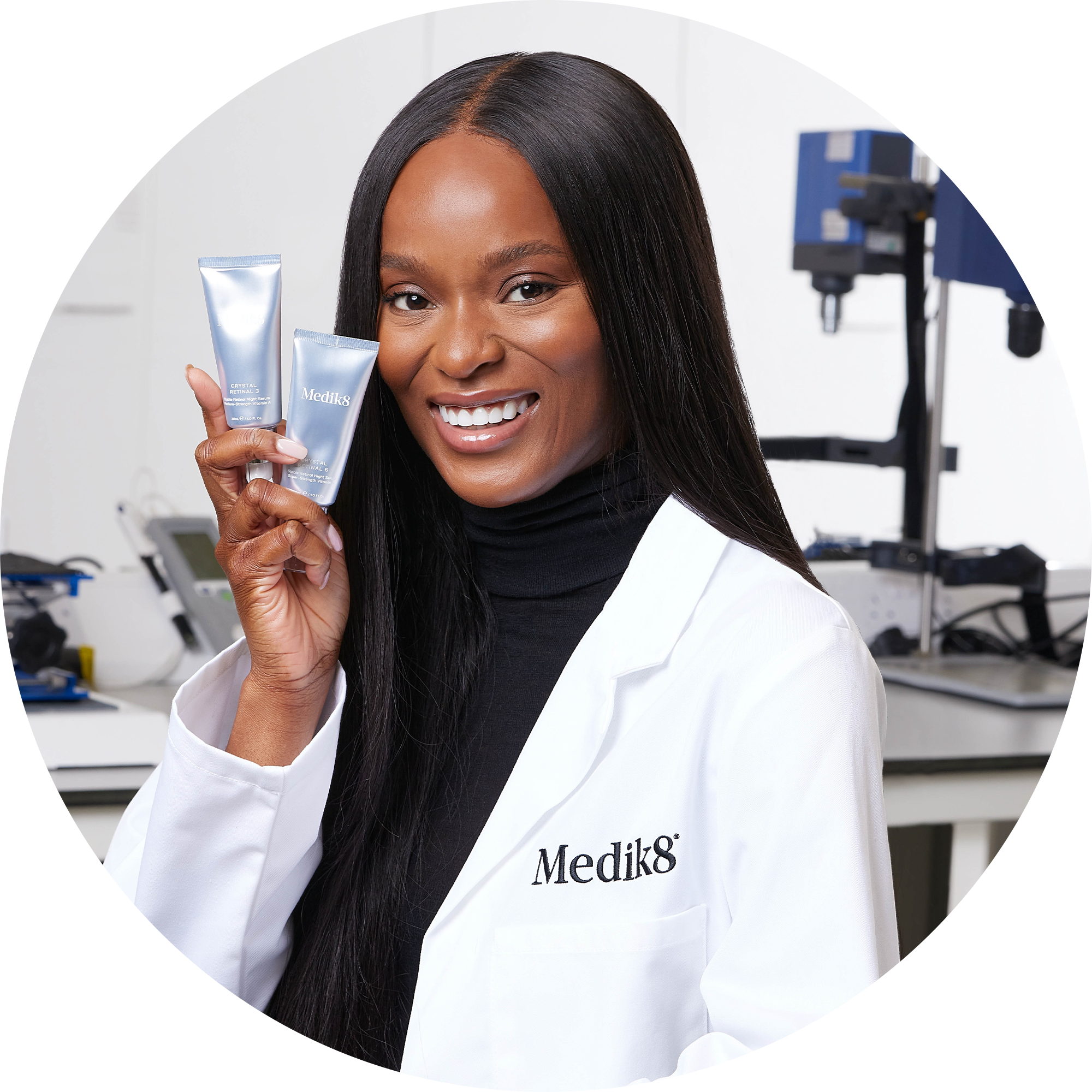 A circular portrait of a smiling skincare professional wearing a branded lab coat, holding two silver Crystal Retinal tubes in a brightly lit laboratory setting.