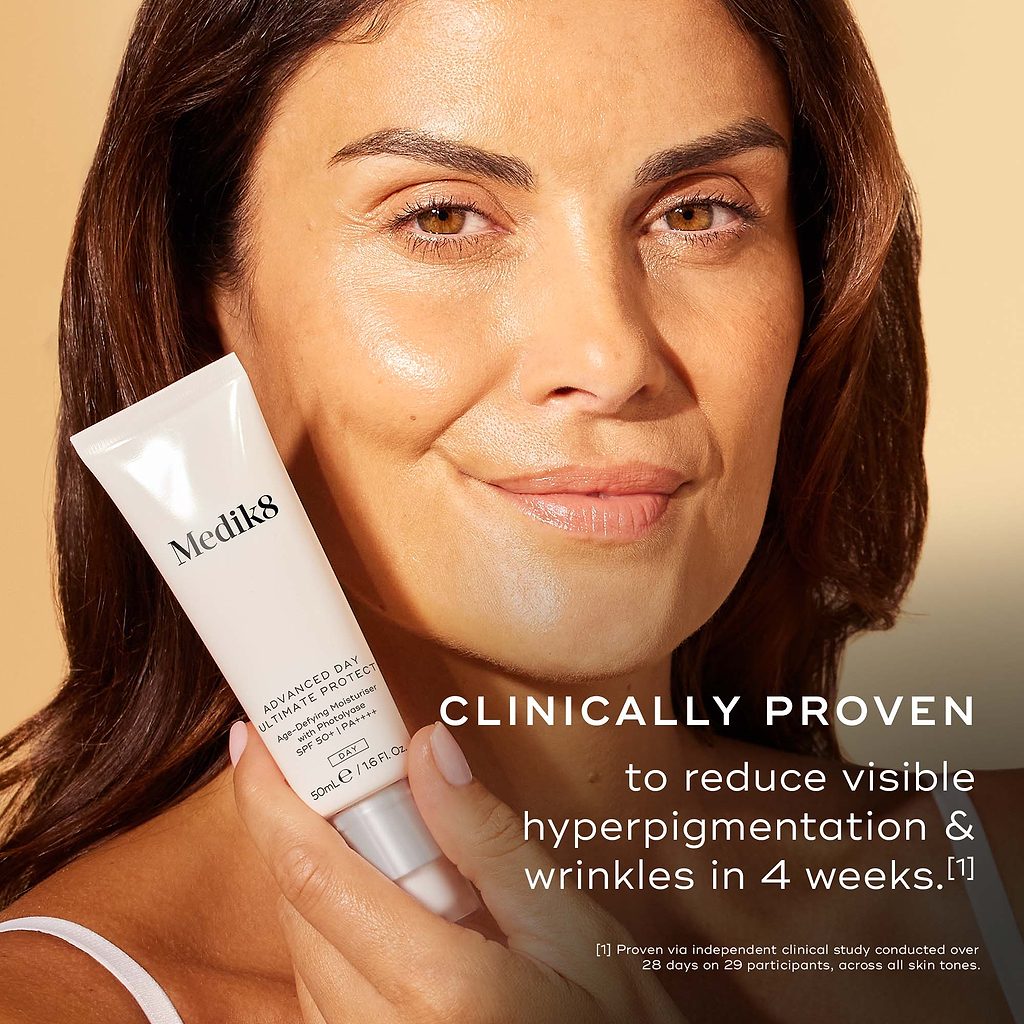 A woman holding a white tube of Medik8 Advanced Day Ultimate Protect SPF 50 sunscreen against a warm beige background, with text reading 'Clinically Proven to reduce visible hyperpigmentation & wrinkles in 4 weeks.'.