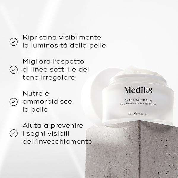 Barattolo di crema Medik8 C-Tetra esposto su un blocco di pietra grigia su uno sfondo bianco con raggi di luce morbida. L’immagine mostra quattro affermazioni con segno di spunta: ripristina visibilmente la radiosità della pelle, migliora l’aspetto delle linee sottili e del tono cutaneo irregolare, nutre e ammorbidisce la pelle, aiuta a prevenire i segni visibili dell’invecchiamento.