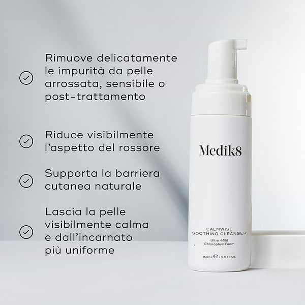 Il flacone di Medik8 Calmwise Soothing Cleanser si trova su un blocco bianco contro uno sfondo grigio chiaro. Il testo in italiano descrive i benefici della schiuma ultra-delicata alla clorofilla, tra cui la rimozione delicata delle impurità dalla pelle arrossata, sensibile o post-trattamento, la riduzione visibile dell'aspetto del rossore, il supporto alla barriera cutanea naturale e il lasciare la pelle visibilmente calma con un incarnato più uniforme.