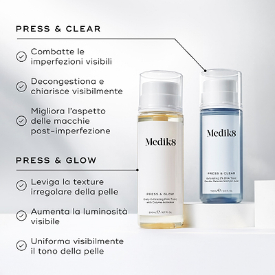 Immagine di confronto che mostra i flaconi Medik8 Press & Glow e Press & Clear affiancati su blocchi espositivi bianchi. Il testo in italiano confronta i loro benefici, notando che Press & Clear combatte le imperfezioni visibili, decongestiona e migliora l'aspetto delle macchie post-imperfezione, mentre Press & Glow leviga la texture irregolare, aumenta la luminosità e uniforma il tono della pelle.