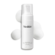 Een pompflacon Medik8 Calmwise Soothing Cleanser getoond op een witte achtergrond met een veeg wit schuim erachter om de textuur van het product te benadrukken.