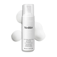 De Medik8 Calmwise Soothing Cleanser-pompfles wordt weergegeven tegen een witte achtergrond met een veeg witte schuimtextuur erachter, wat de textuur van het product benadrukt.