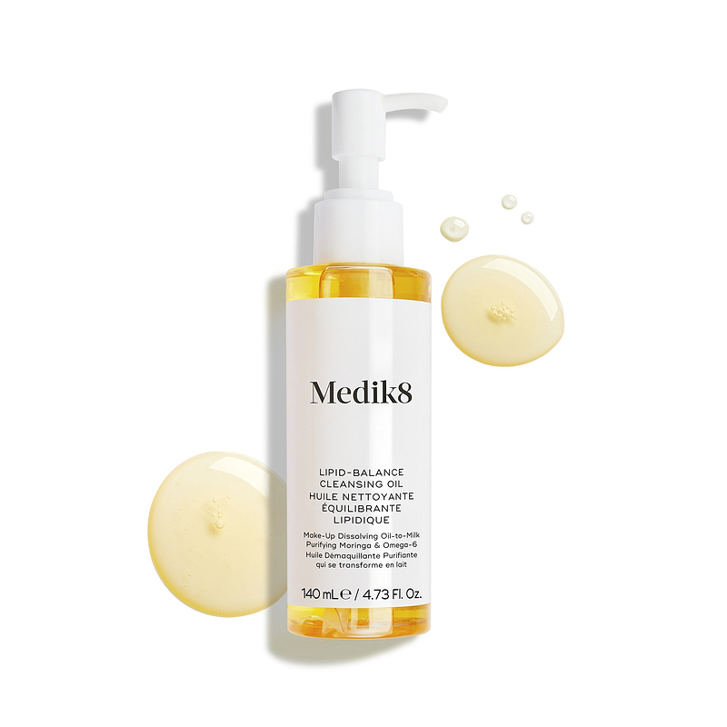 De flacon van Medik8 Lipid-Balance Cleansing Oil staat tegen een witte achtergrond. Gouden oliedruppels omringen de flacon en benadrukken de rijke, vloeibare textuur.