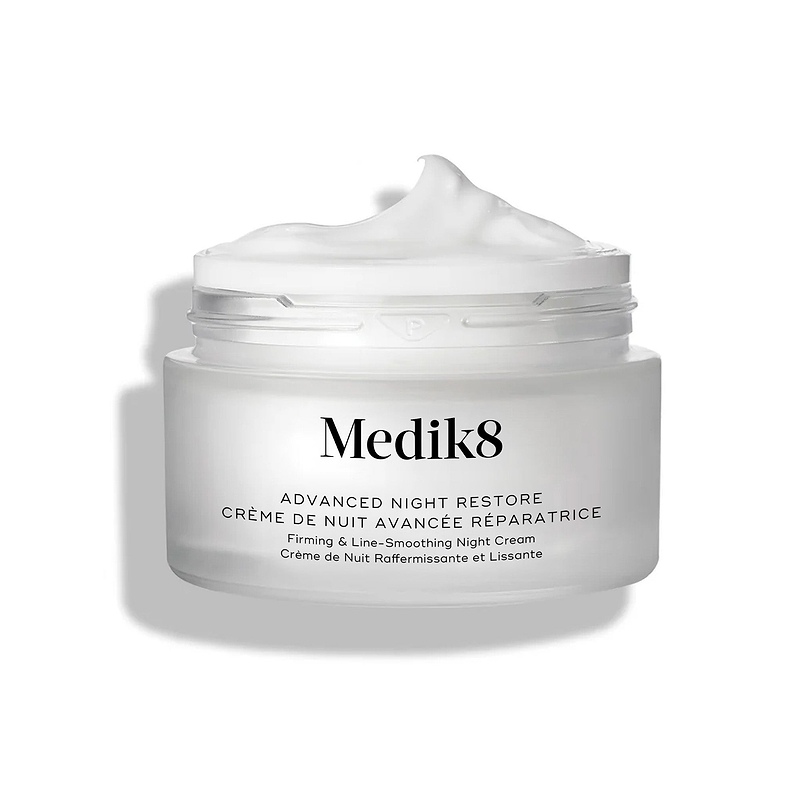 De geopende pot Medik8 Advanced Night Restore toont een rijke toef witte crème met een zachte piek tegen een strakke witte achtergrond, waardoor de gladde, herstellende textuur wordt benadrukt. De zwarte tekst op de pot luidt: "Rejuvenating Multi-Ceramide Night Cream."