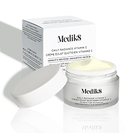De geopende pot Daily Radiance Vitamin C met de deksel ligt ervoor, met de productverpakking op de achtergrond. De afbeelding toont de rijke textuur van de crème.