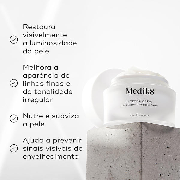 Um pote aberto de Medik8 C-Tetra Cream assenta num bloco de betão texturizado contra um fundo claro. O texto em português lista os benefícios: restaura visivelmente a luminosidade da pele, melhora a aparência de linhas finas e da tonalidade irregular, nutre e suaviza a pele e ajuda a prevenir sinais visíveis de envelhecimento.