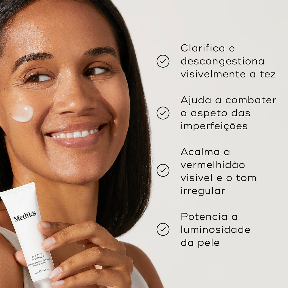 Uma mulher sorridente com um pouco de creme na bochecha segura o tubo Clarity Peptides contra um fundo claro. Os marcadores listam os seus benefícios: clarifica e descongestiona visivelmente a tez, ajuda a combater o aspeto das imperfeições, acalma a vermelhidão visível e o tom irregular, e potencia a luminosidade da pele.