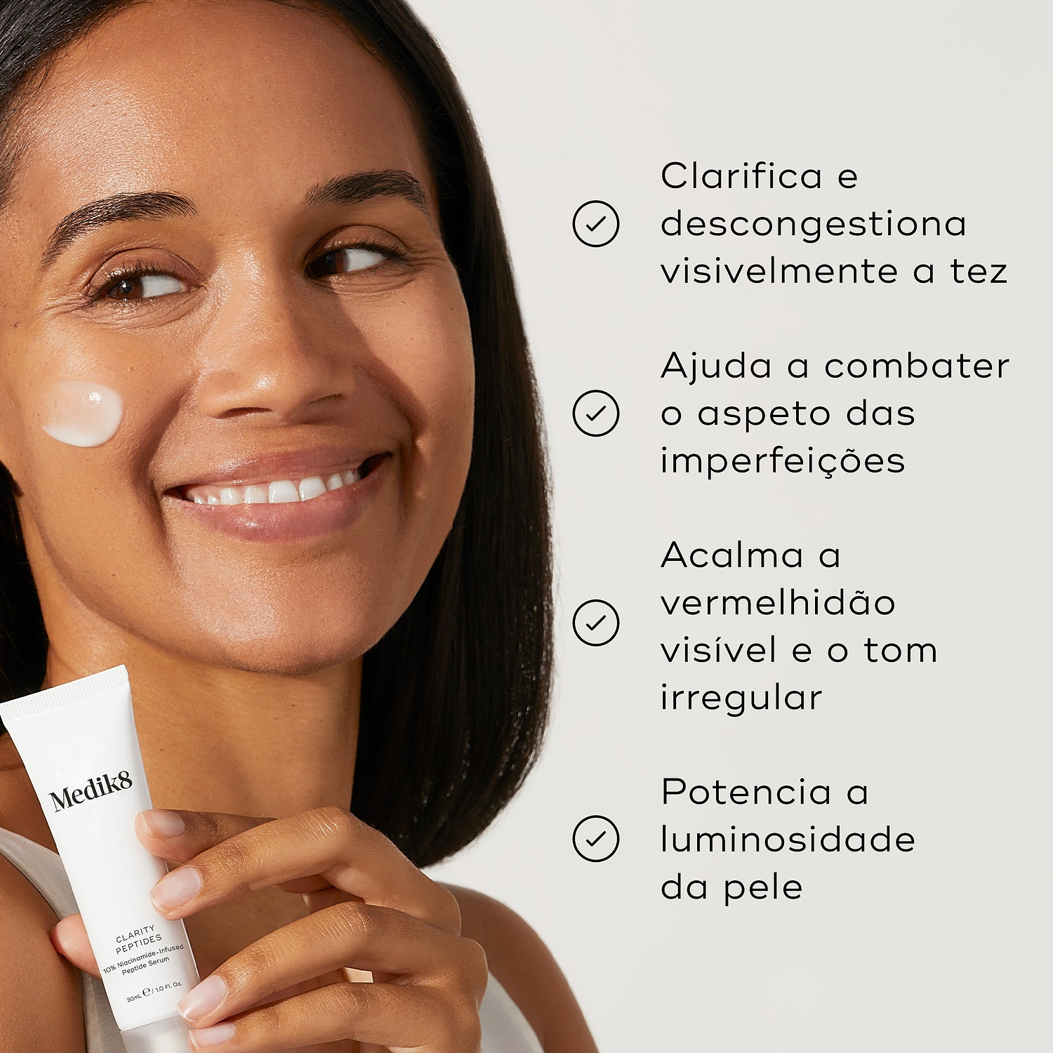 Uma mulher sorridente com um pouco de creme na bochecha segura o tubo Clarity Peptides contra um fundo claro. Os marcadores listam os seus benefícios: clarifica e descongestiona visivelmente a tez, ajuda a combater o aspeto das imperfeições, acalma a vermelhidão visível e o tom irregular, e potencia a luminosidade da pele.