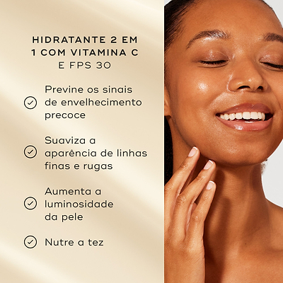Uma mulher sorridente toca o seu rosto luminoso contra um fundo bege quente. Intitulado "HIDRATANTE 2 EM 1 COM VITAMINA C E FPS 30", os marcadores listam os benefícios: previne os sinais de envelhecimento precoce, suaviza a aparência de linhas finas e rugas, aumenta a luminosidade da pele, e nutre a tez.