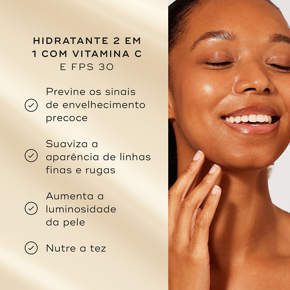 Uma mulher sorridente toca o seu rosto luminoso contra um fundo bege quente. Intitulado "HIDRATANTE 2 EM 1 COM VITAMINA C E FPS 30", os marcadores listam os benefícios: previne os sinais de envelhecimento precoce, suaviza a aparência de linhas finas e rugas, aumenta a luminosidade da pele, e nutre a tez.