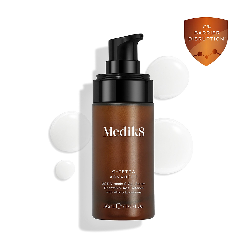 O frasco do sérum Medik8 C-Tetra Advanced é exibido sobre um fundo branco limpo com gotas de sérum translúcidas, destacando sua textura leve de sérum em gel. Um ícone de escudo laranja no canto destaca "0% INTERRUPÇÃO DA BARREIRA".
