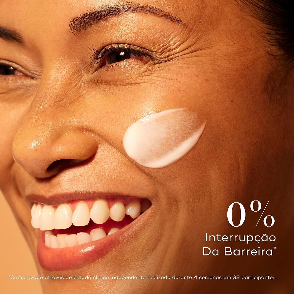 Close-up de uma mulher sorrindo com uma mancha de creme branco na bochecha. O texto afirma "0% Interrupção Da Barreira", observando que foi comprovado através de um estudo clínico independente de 4 semanas com 32 participantes.
