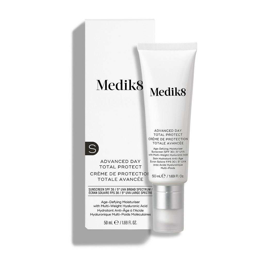 Uma bisnaga branca de Medik8 Advanced Day Total Protect está colocada ao lado da sua embalagem de cartão branca correspondente.