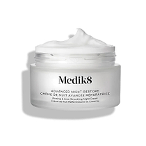 Frasco do creme Medik8 Advanced Night Restore aberto, com uma generosa quantidade de creme branco em relevo no topo, sobre um fundo branco limpo, destacando a sua textura suave e restauradora.