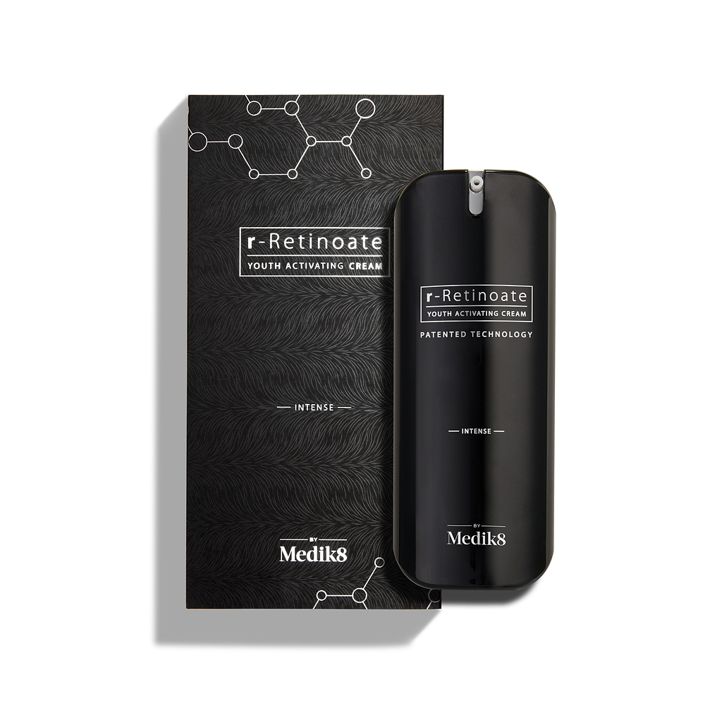 Fľaštička Medik8 r-Retinoate Intense Youth Activating Cream stojí vedľa svojho čierneho vonkajšieho obalu s bielymi hexagonálnymi chemickými štruktúrami a textúrovaným vlnitým vzorom.
