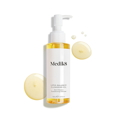 Medik8 Lipid-Balance Cleansing Oil bottle stands against a white background. Golden oil droplets surround the bottle, highlighting its rich, fluid texture.