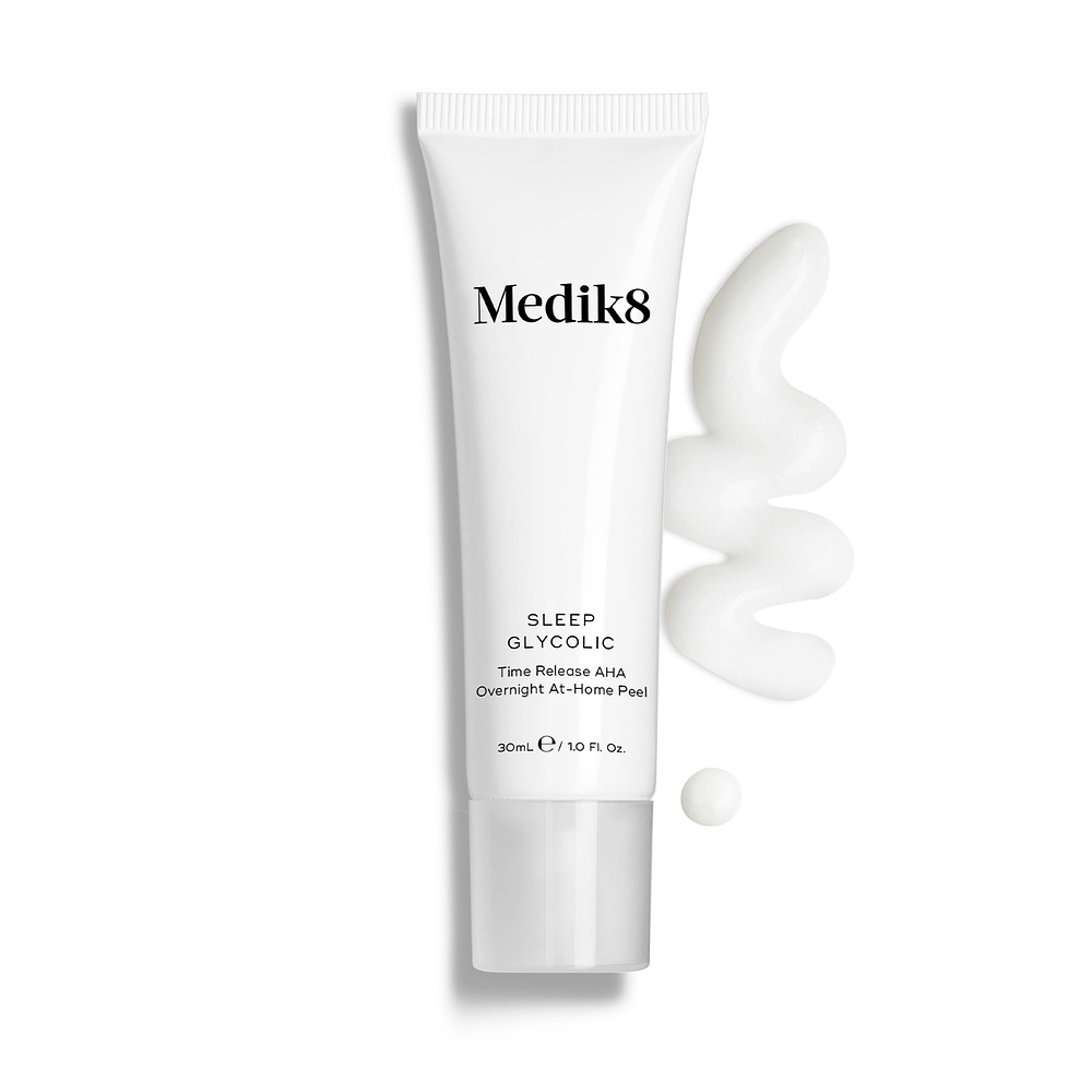 Medik8 Sleep Glycolic tube stands against a clean white background with a wavy swipe and a small droplet of white cream texture. Text identifies the product as a Time Release AHA Overnight At-Home Peel in a 30mL size.
