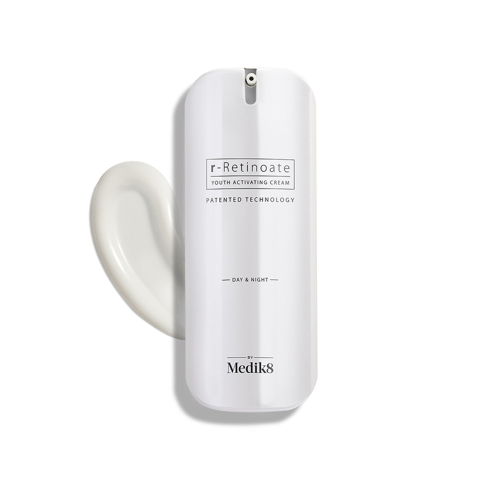 A sleek white pump bottle of r-Retinoate Day & Night stands upright, with a swirl of white cream next to it.