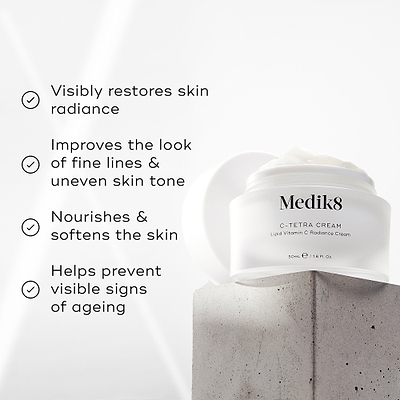 Medik8 C-Tetra Cream jar displayed on a grey stone block against a white background with soft light rays. The image features four check-marked claims: Visibly restores skin radiance, Improves the look of fine lines & uneven skin tone, Nourishes & softens the skin and Helps prevent visible signs of ageing