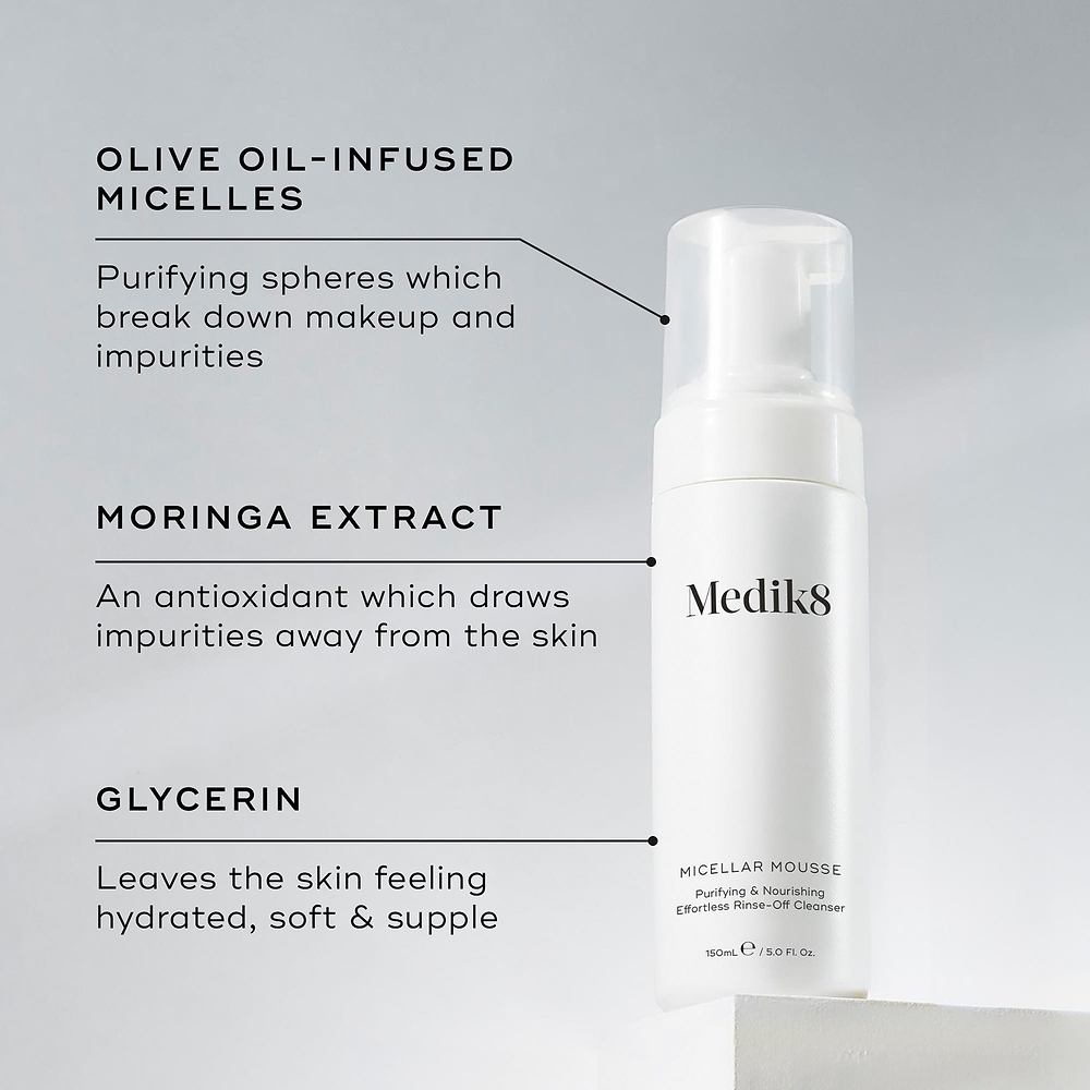 A Medik8 Micellar Mousse bottle displayed on a white block. Lines connect the bottle to text explaining key ingredients: "Olive Oil-Infused Micelles" to break down makeup, "Moringa Extract" to draw out impurities, and "Glycerin" for hydration.