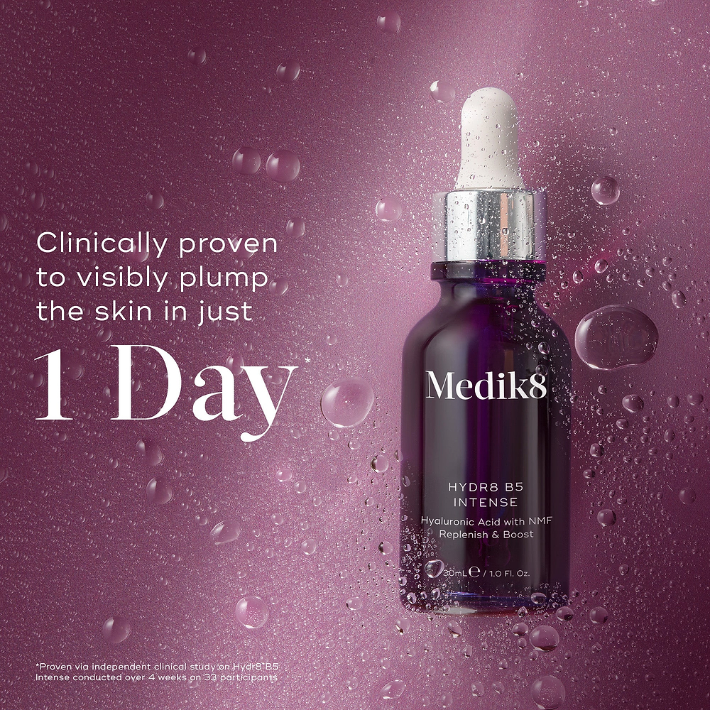 Medik8 Hydr8 B5 Intense glass dropper bottle centered on a shimmering purple background with translucent water droplets. Bold text states the product is clinically proven to visibly plump the skin in just 1 Day.