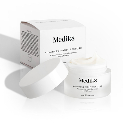 Medik8 Advanced Night Restore cream jar sits open with its white lid leaning against it and the product box behind. The image showcases the rich texture of the cream and the clean packaging design.