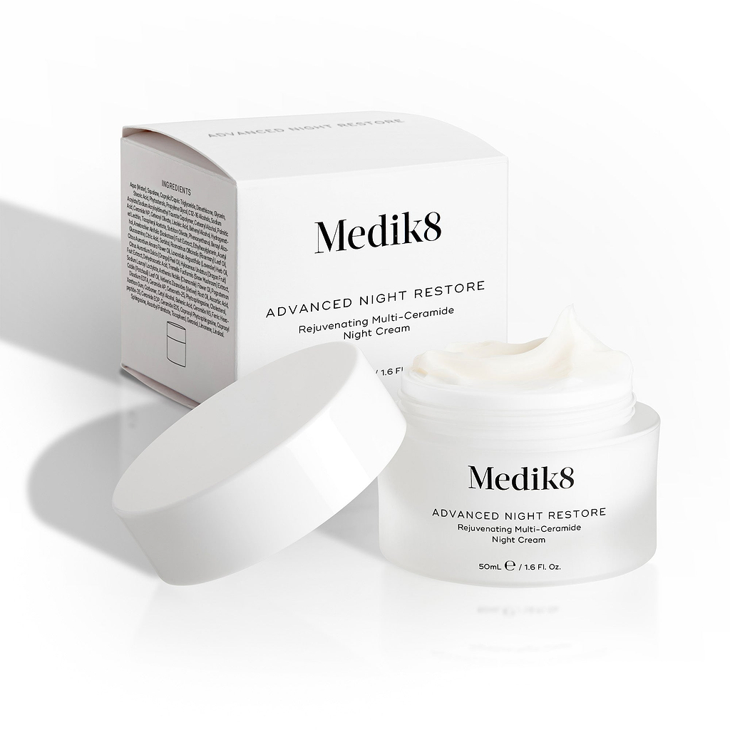 Medik8 Advanced Night Restore cream jar sits open with its white lid leaning against it and the product box behind. The image showcases the rich texture of the cream and the clean packaging design.
