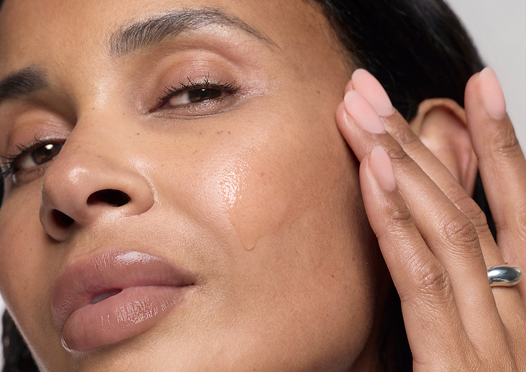 Close-up of a woman's face with one hand gently touching her cheek and swatch of Exo-PDRN Prismatic+ on the skin