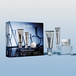 Medik8 Nighttime Reset gift set displayed against a light blue gradient background. A silver Crystal Retinal 3 pump tube, Crystal Retinal Ceramide Eye 3 tube, and Advanced Night Restore mini cream jar are arranged on transparent blocks beside their blue branded box, which features faint imagery of laboratory glassware. The box text lists the kit contents.