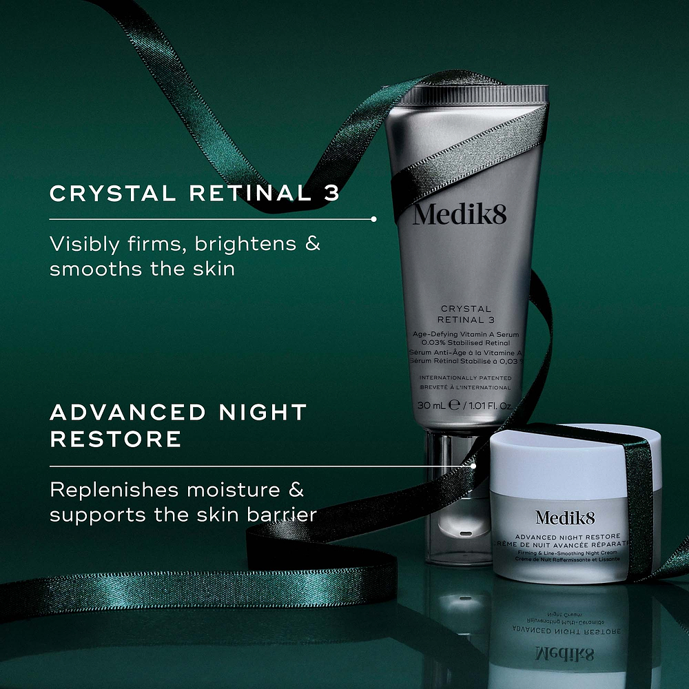 Two Medik8 products wrapped in a green ribbon against a dark green background, with text highlighting key benefits for each. The Crystal Retinal 3 tube "Visibly firms, brightens & smooths the skin," and the Advanced Night Restore travel size jar "Replenishes moisture & supports the skin barrier."