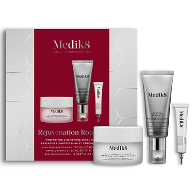A Medik8 "Rejuvenation Routine" gift box displayed on a white background with a deep red center and hexagonal graphics, showing the printed products inside. A Daily Radiance Vitamin C jar, Crystal Retinal 3 tube, and Exo-PDRN Prismatic+ deluxe sample stand loose beside the box.