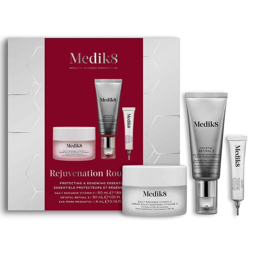 A Medik8 "Rejuvenation Routine" gift box displayed on a white background with a deep red center and hexagonal graphics, showing the printed products inside. A Daily Radiance Vitamin C jar, Crystal Retinal 3 tube, and Exo-PDRN Prismatic+ deluxe sample stand loose beside the box.
