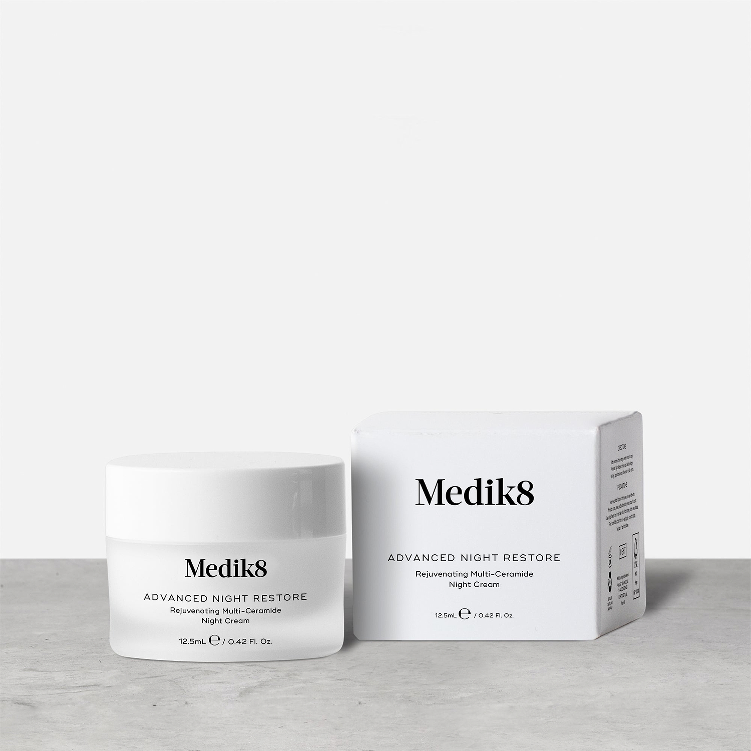 A travel-size jar (12.5ml) of Medik8 Advanced Night Restore cream displayed closed next to its box on a textured grey surface. Text identifies it as a "Rejuvenating Multi-Ceramide Night Cream."