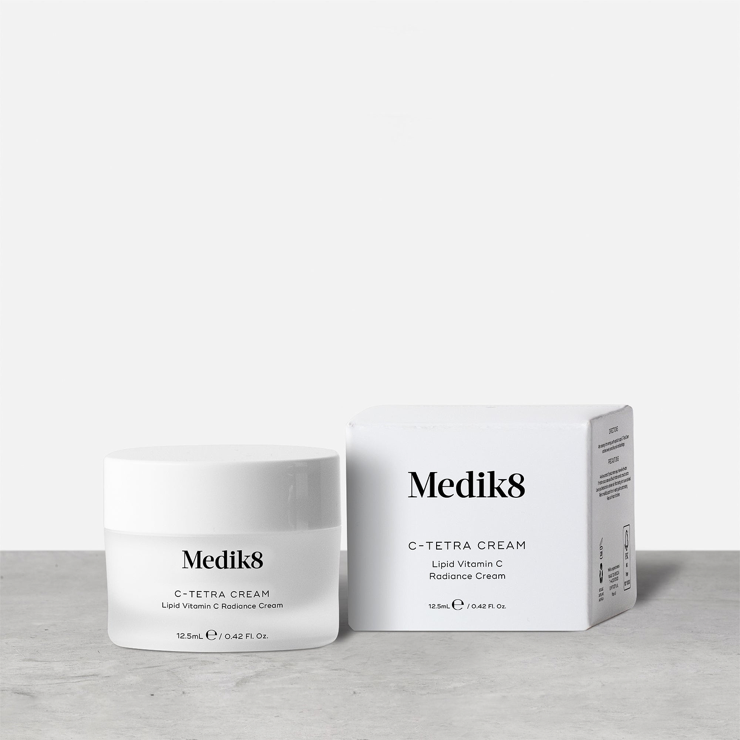 A 12.5ml white jar of Medik8 C-Tetra Cream, labeled "Lipid Vitamin C Radiance Cream," stands next to its corresponding white packaging box on a grey surface against a clean white background.