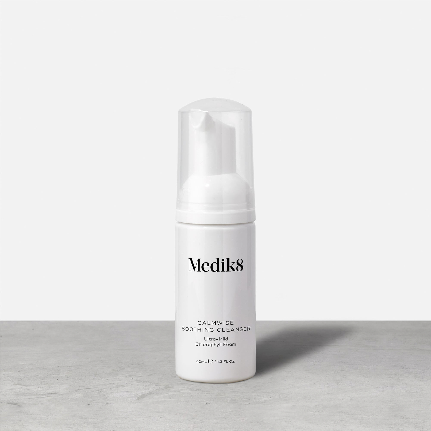 A travel-size pump bottle (40ml) of Medik8 Calmwise Soothing Cleanser displayed on a grey surface. Text describes it as an "Ultra-Mild Chlorophyll Foam."