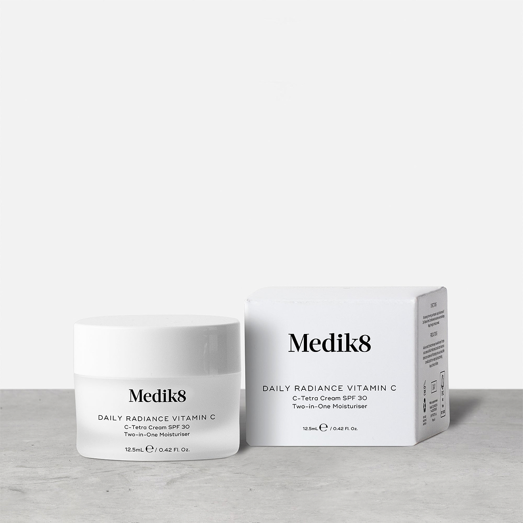 A 12.5ml white jar of Medik8 Daily Radiance Vitamin C, labeled 'C-Tetra Cream SPF 30 Two-in-One Moisturiser,' stands next to its corresponding white cardboard box on a grey surface against a clean white background.