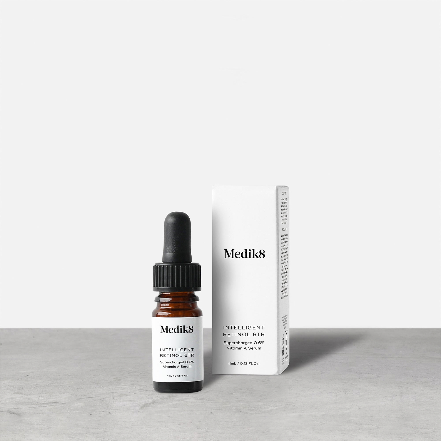 Medik8 Intelligent Retinol 6TR Travel Sized serum bottle stands next to its matching white product carton on a grey textured surface against a neutral background. Text on the 4mL bottle identifies it as a "Supercharged 0.6% Vitamin A Serum."