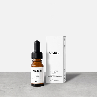 An 8ml brown glass dropper bottle of Medik8 C-Tetra Luxe serum stands next to its white packaging box on a grey surface against a white background. Text on both reads: "Medik8, C-TETRA LUXE, Lipid Vitamin C Enhanced Radiance Serum, 8mL e / 0.27 Fl. Oz.".
